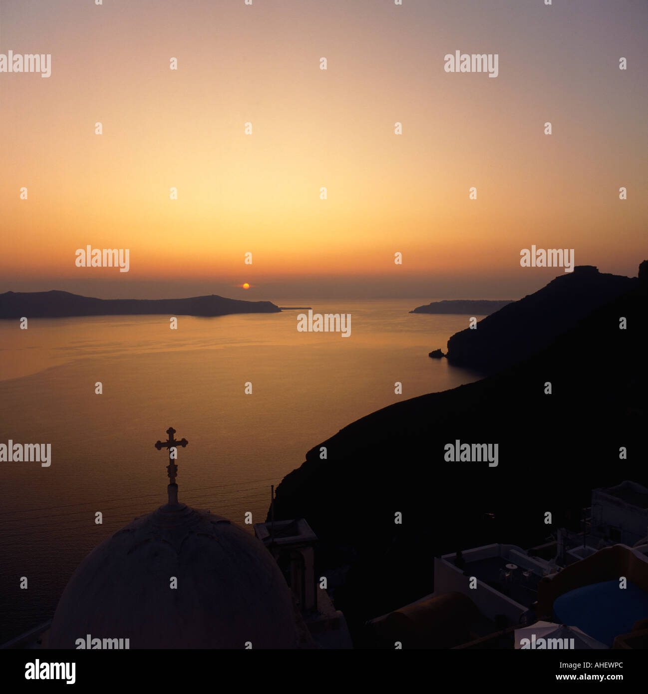 Sunset over the domed church of Fira with cross atop looking towards Thirasia on Santorini The Greek Islands Stock Photo