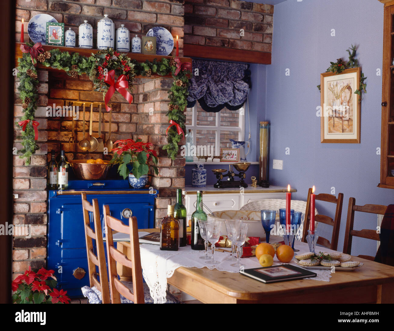 Ivy garland above brick fireplace with blue Rayburn oven in blue country kitchen with table set for Christmas lunch Stock Photo