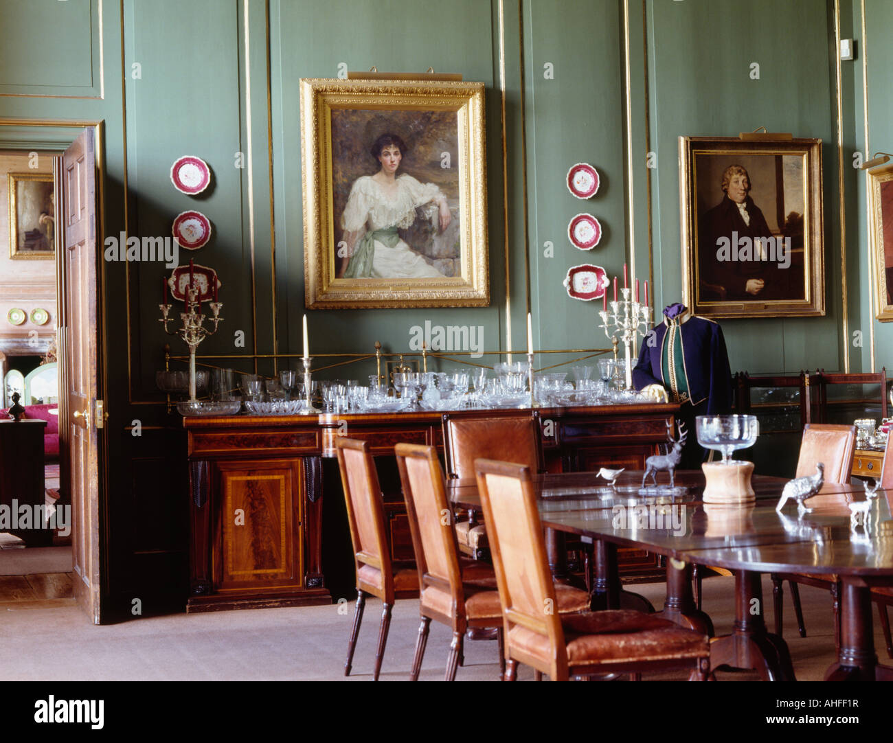 Paintings on green panelled walls in Georgian dining room with antique chairs and table Stock Photo