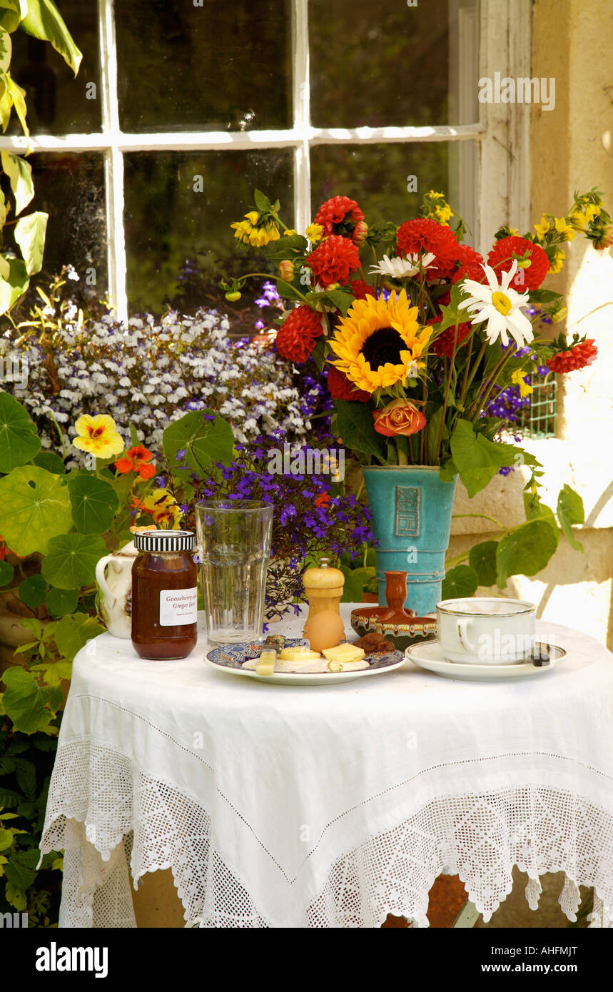 White lace cloth on table and vase of summer flowers on table set for tea outside window with
