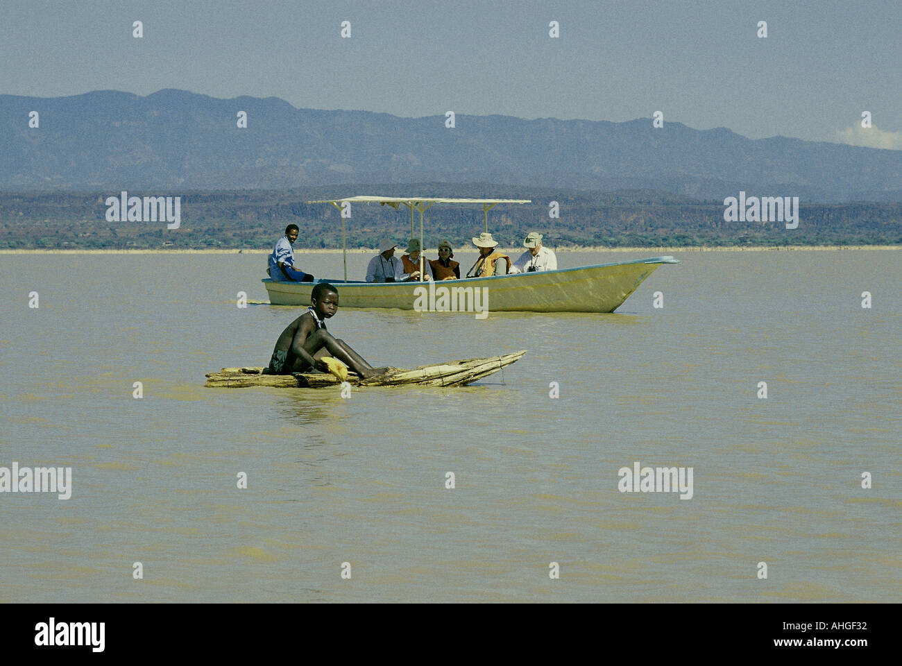 Tourists in a motor boat near young Njemps boy riding on his Ambach canoe on Lake Baringo in the Great Rift Valley Kenya East Stock Photo
