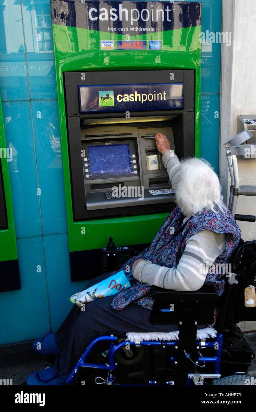 Elderly wheelchair user withdrawing cash from Lloyds Bank cashpoint, UK Stock Photo