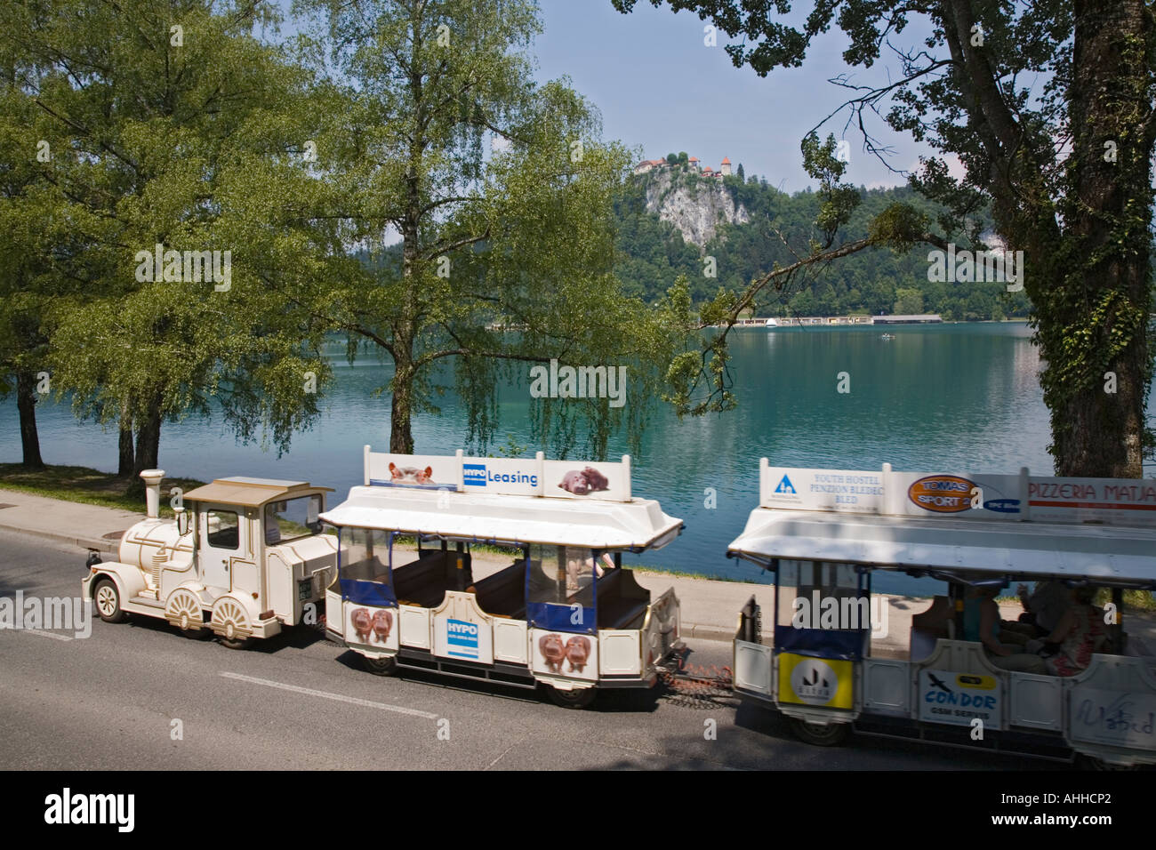 Tourist road train by Lake Bled in summer and Castle on cliff across blue  green water Stock Photo - Alamy
