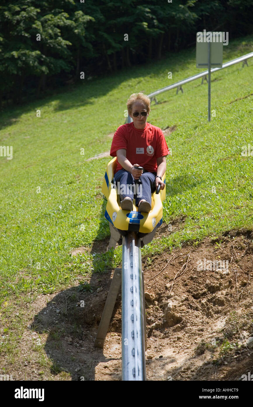 Lady sat riding on yellow sled coming down summer toboggan ride on