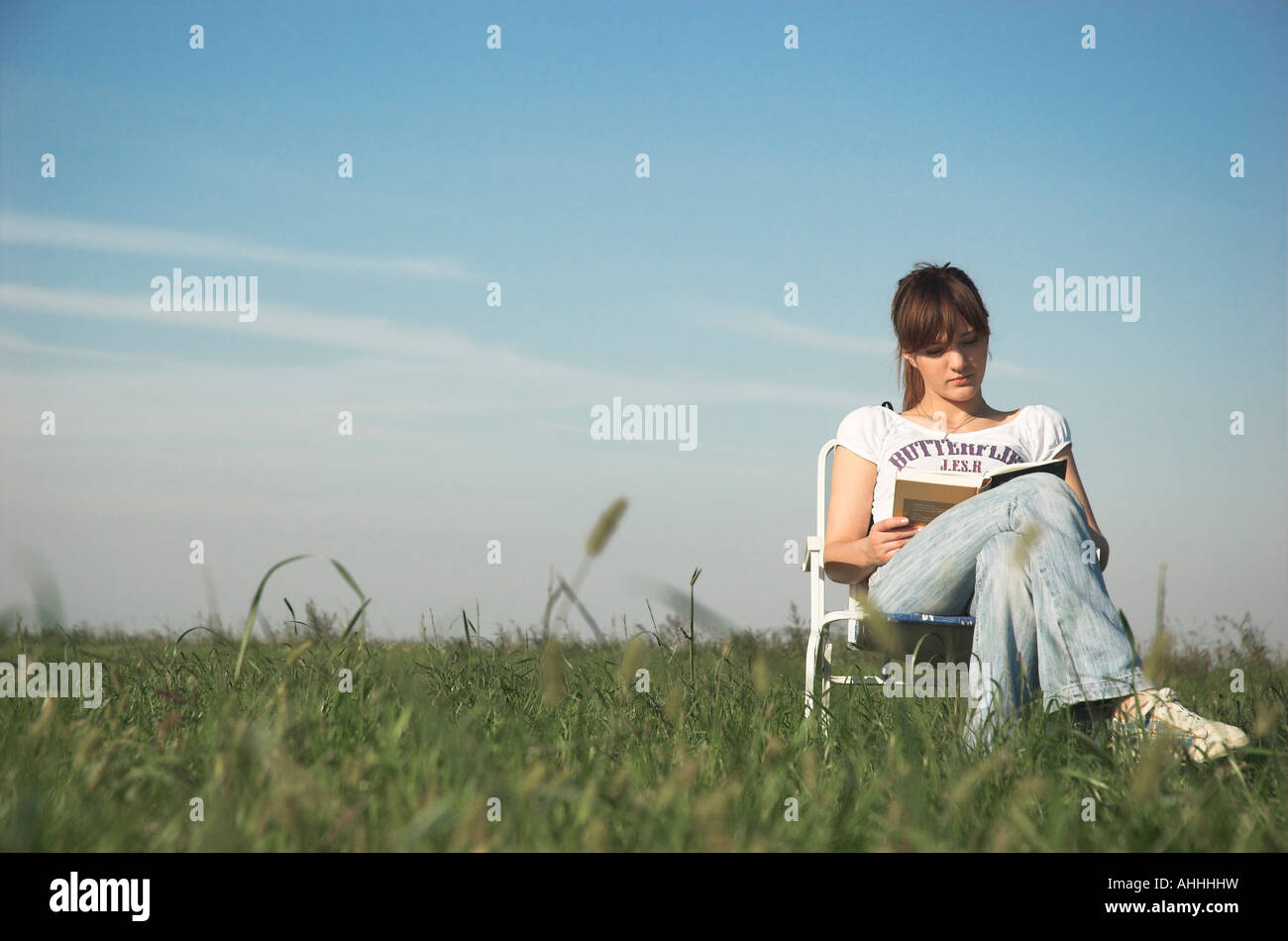 Young woman sitting on chair outdoors reading book Stock Photo - Alamy