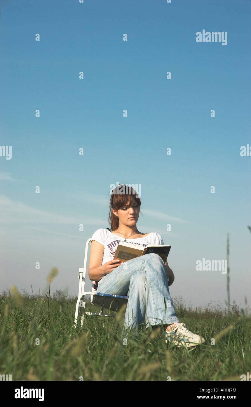Young woman sitting on chair outdoors reading book Stock Photo - Alamy