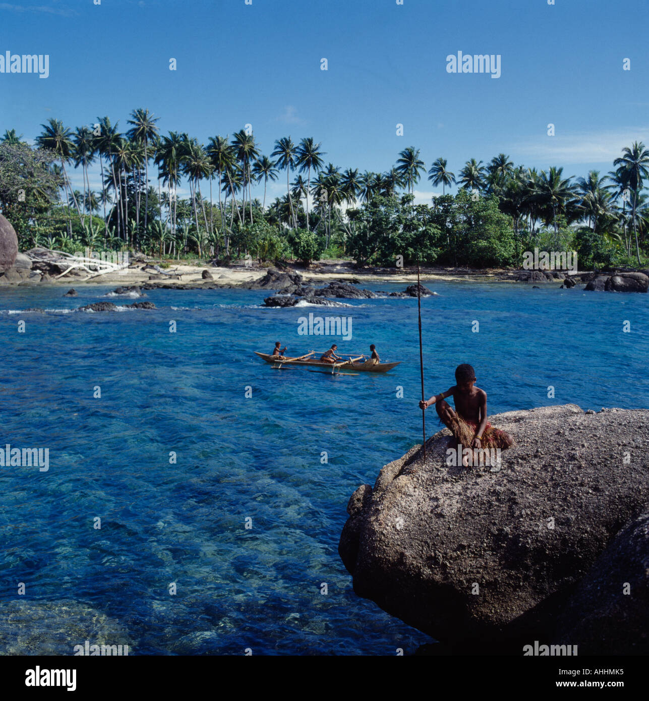 INDONESIA Asia Irian Jaya Sorong Children in outrigger canoe on clear blue water among rocks close to coconut tree lined shore Stock Photo