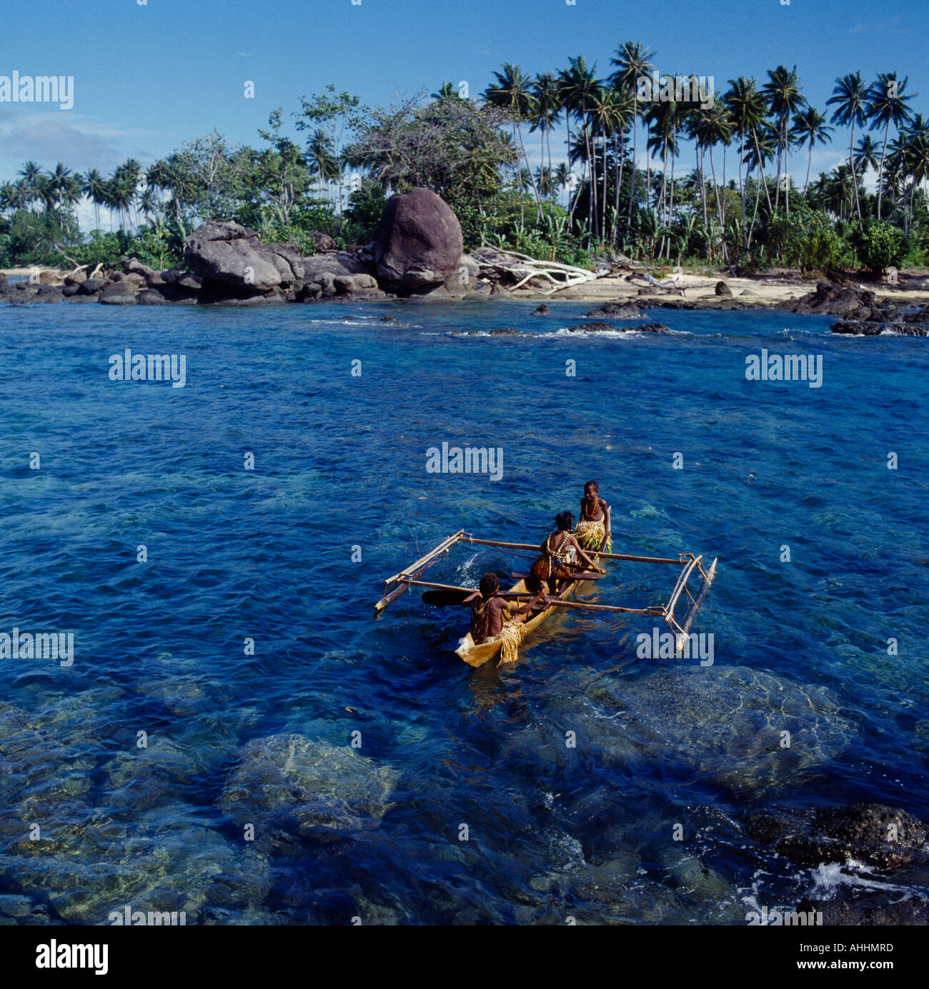 INDONESIA Asia Irian Jaya Sorong Children in outrigger canoe on clear blue water among rocks close to coconut tree lined shore. Stock Photo