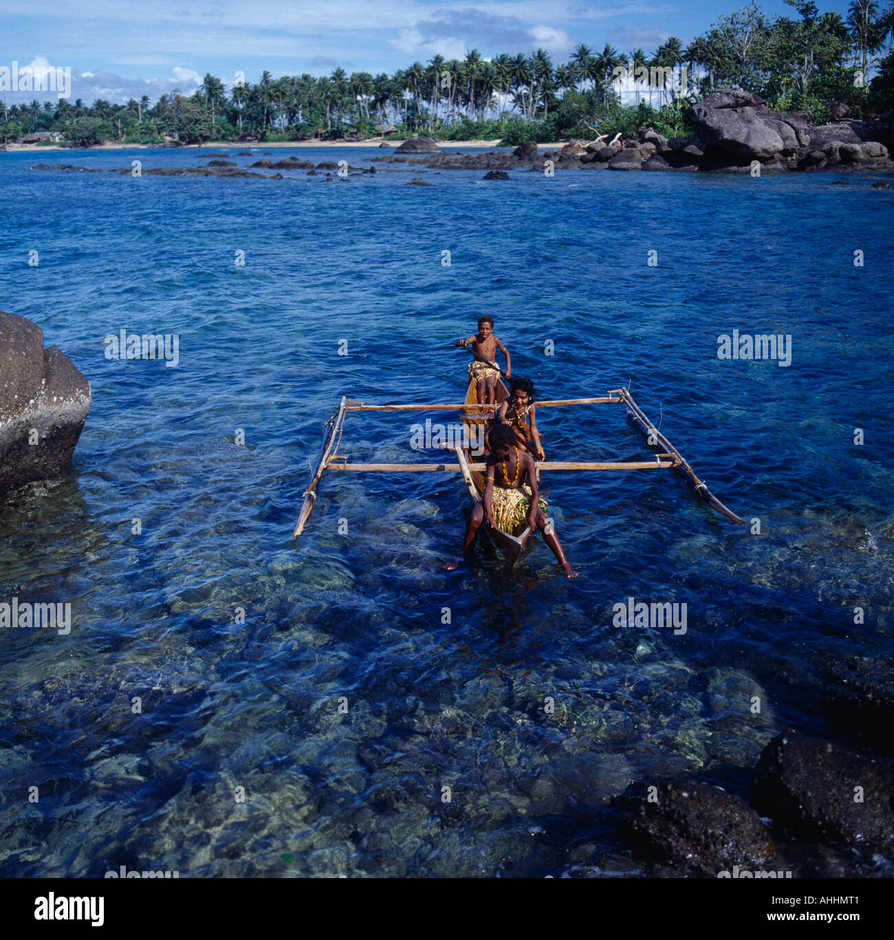 INDONESIA Asia Irian Jaya Sorong Children in outrigger canoe on clear blue water among rocks close to coconut tree lined shore. Stock Photo