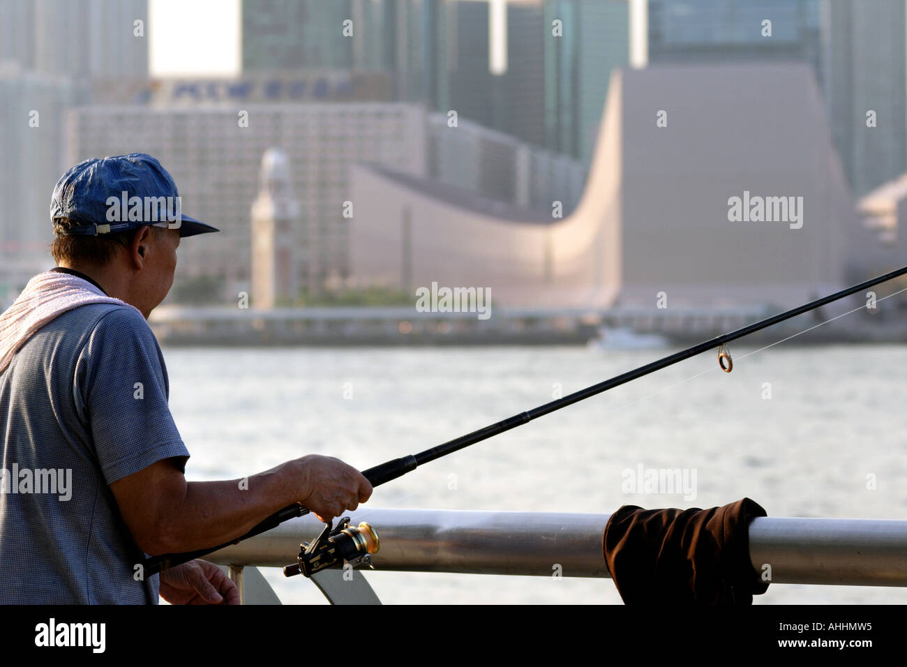 Local Man Fishing Across Victoria Harbour from the Cultural Centre, TST, Hong Kong, China Stock Photo