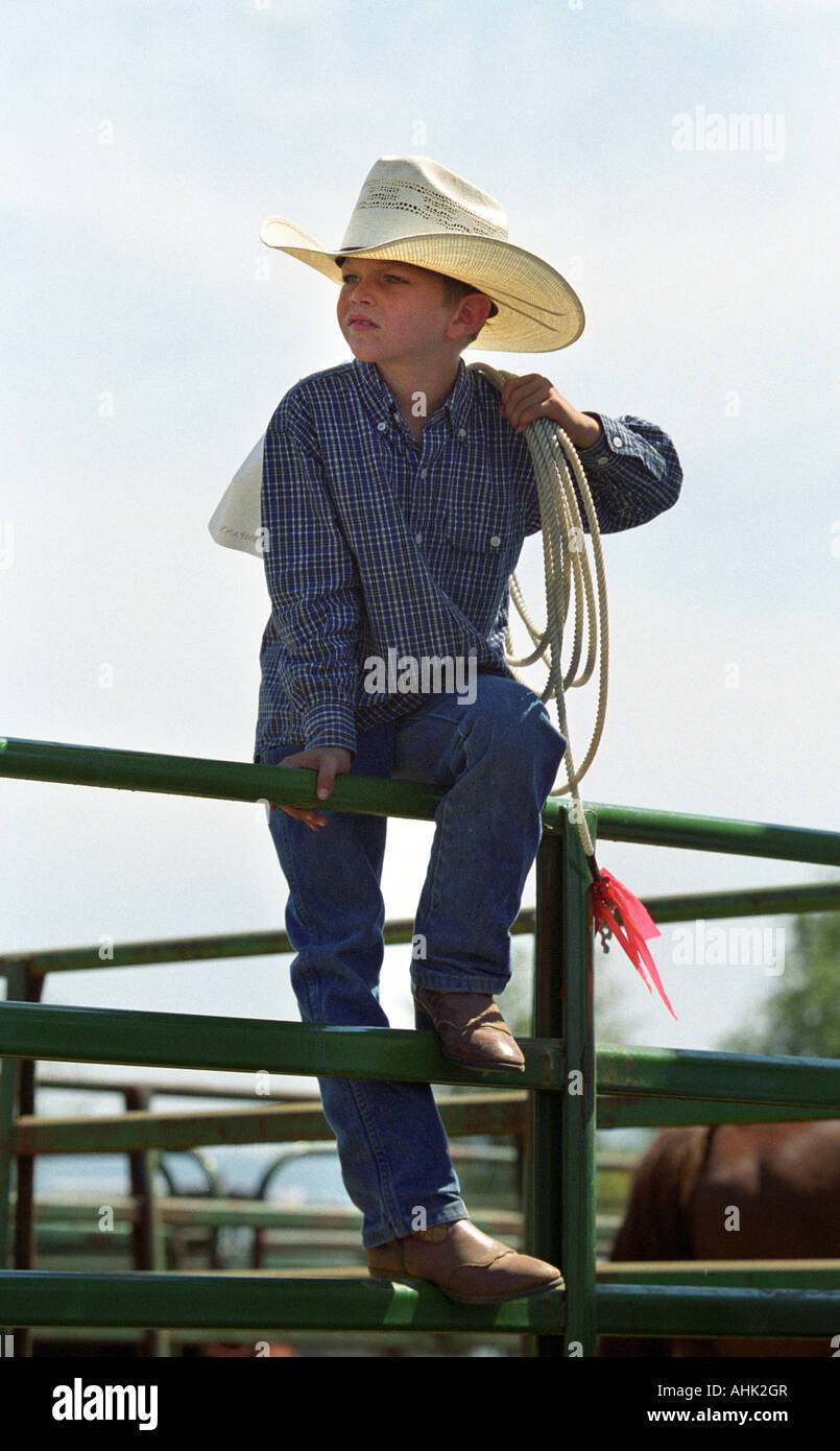 Young rodeo competitor sits on fence with rope over shoulder Stock Photo