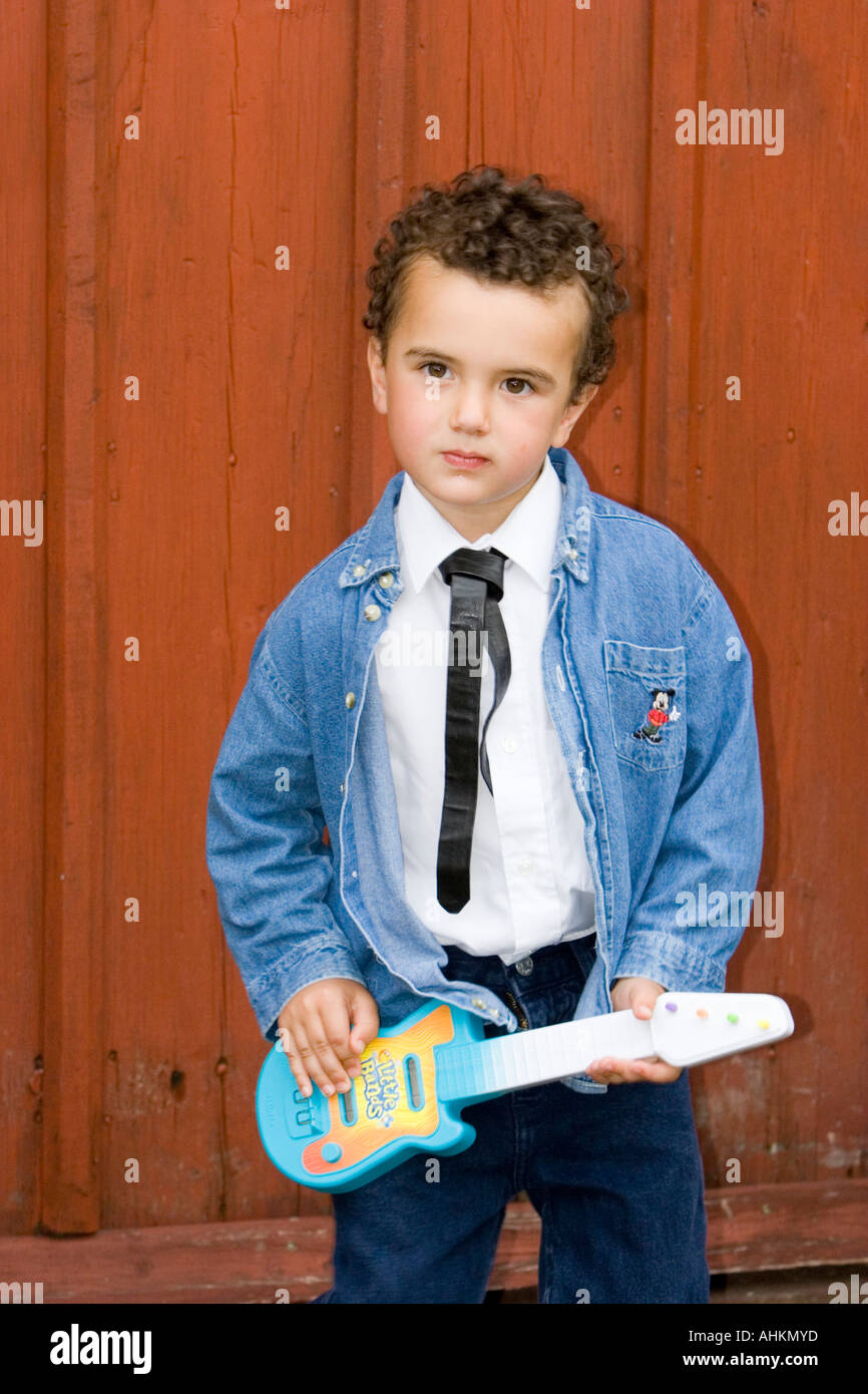 Young boy wearing 1950s outfit of shirt black tie and denim jacket playing a toy guitar Stock Photo