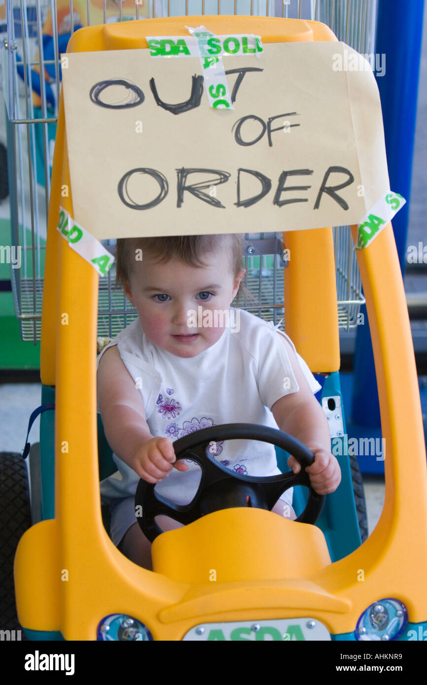Little girl hopefully sits in plastic toy car with sign saying Out of Order Stock Photo