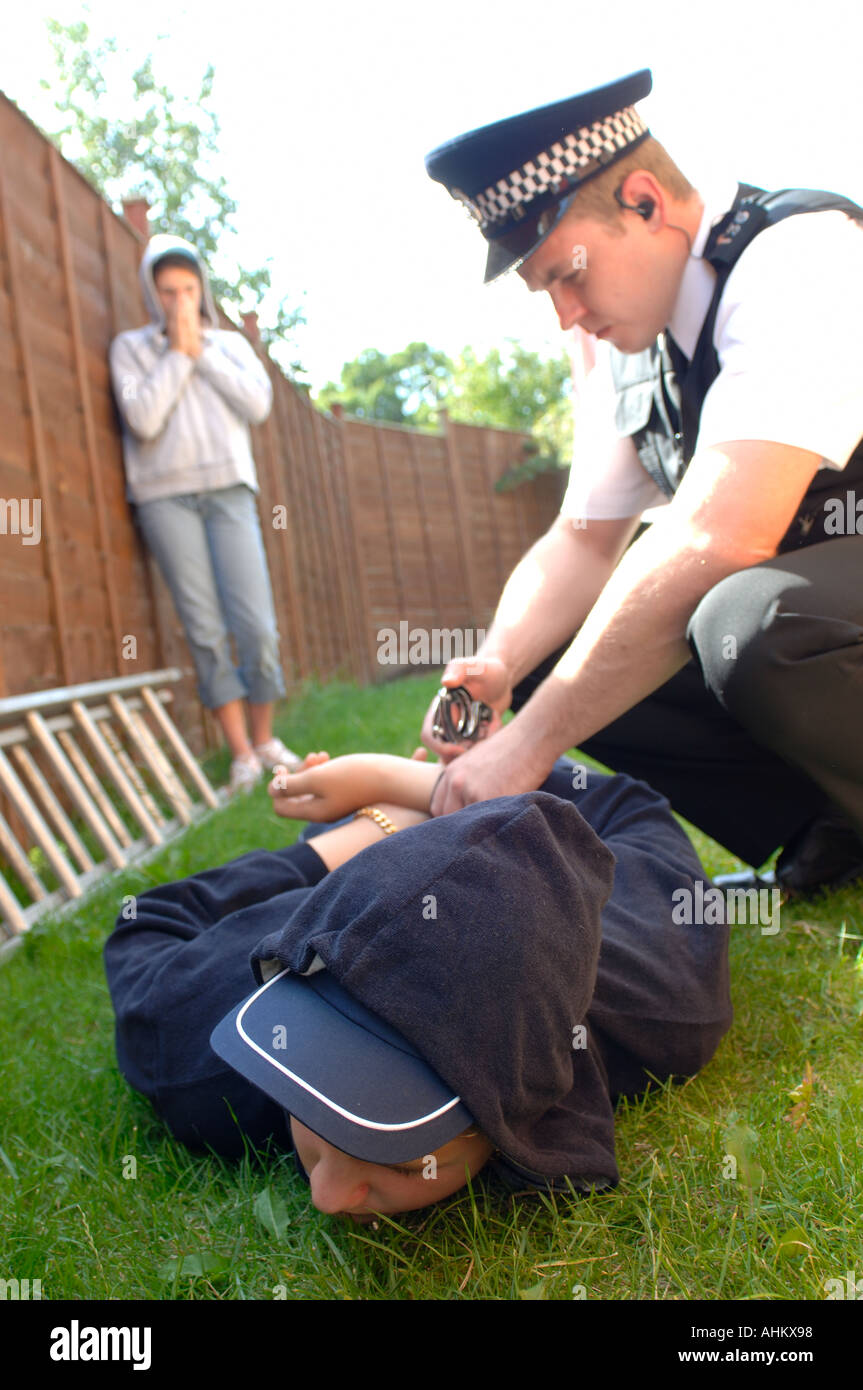 a teenage boy and girl dressed as a chav in a hooded top being searched and questioned and arrested by a police officer Stock Photo