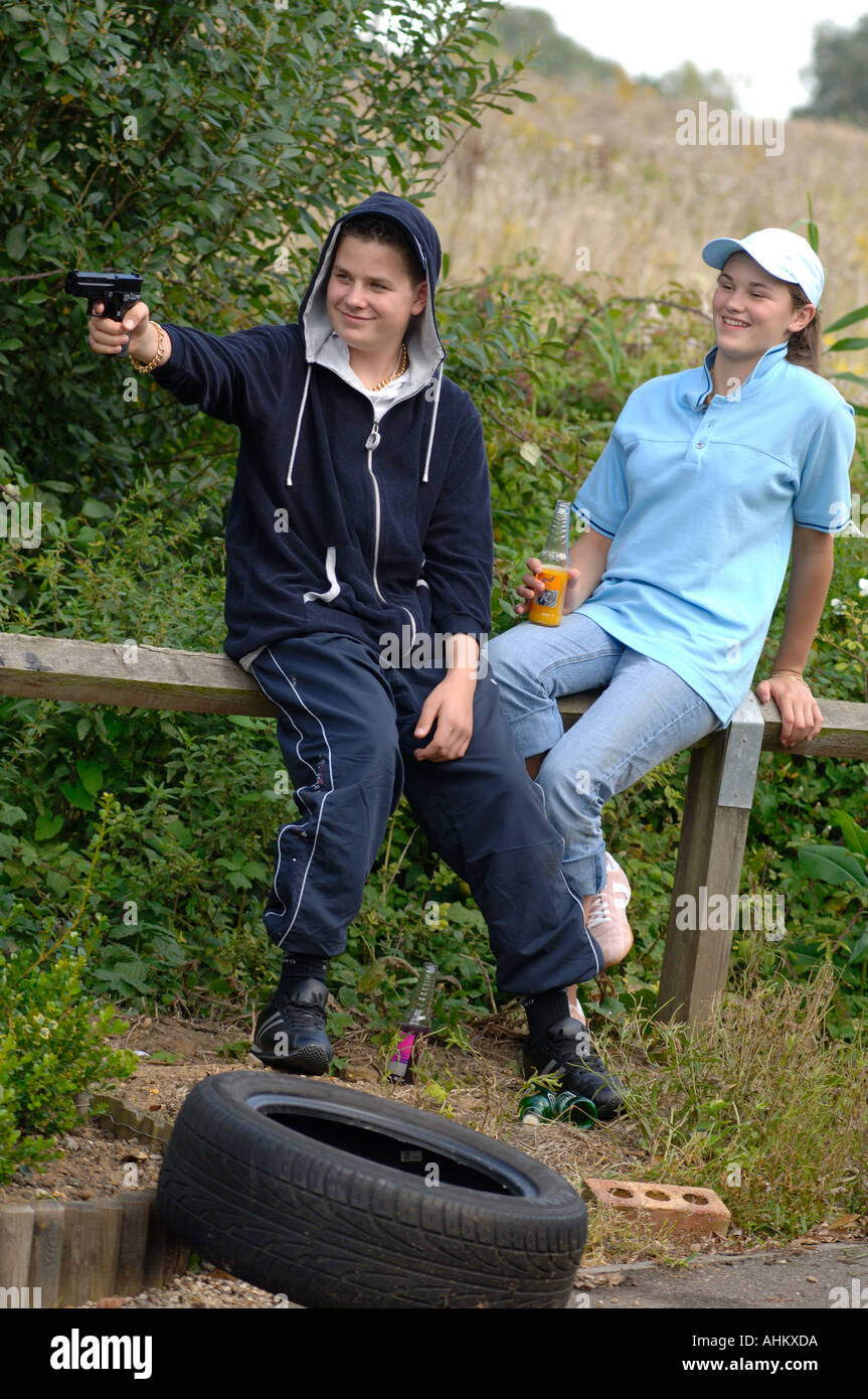 a teenage boy and girl dressed as chavs messing around and drinking alcohol on waste ground pretending to shoot a replica bb gun Stock Photo