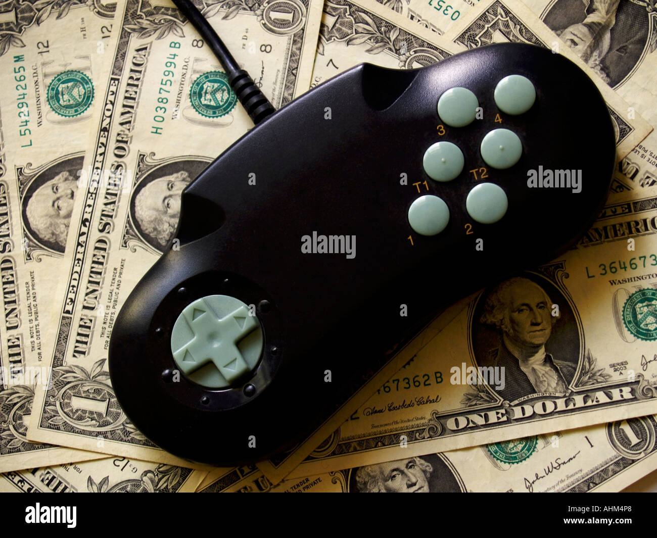 Black and cyan video game console controller against a background of dollar bills Stock Photo