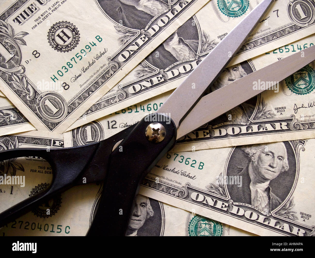 Sharpened black handled scissors against a background of dollar bills Stock Photo