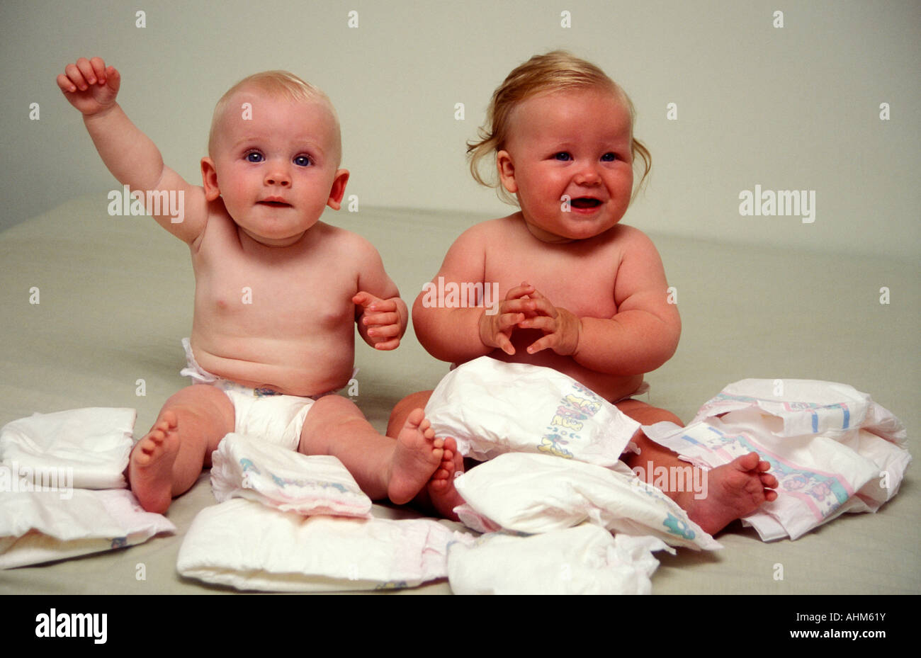 2 little babies sitting together surrounded by disposable nappies diapers Stock Photo