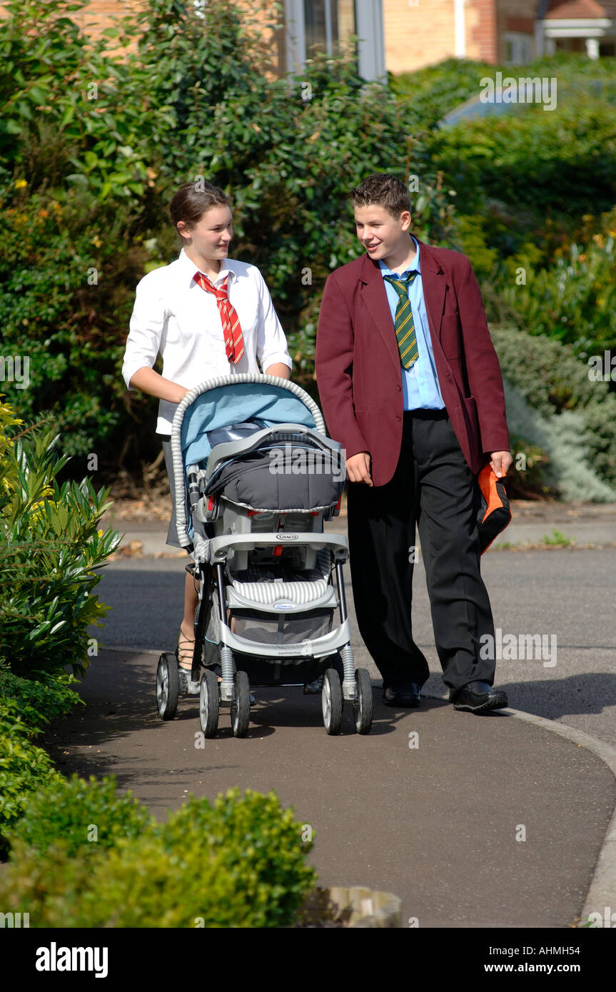 a teenage boy and girl dressed in their school uniforms walking their baby in a pram Stock Photo