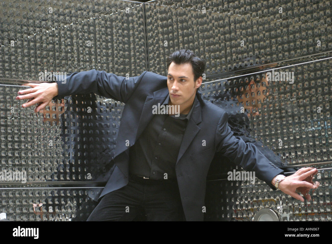 Tall dark handsome Male model posing in front of mirrored wall looking James Bondy Stock Photo