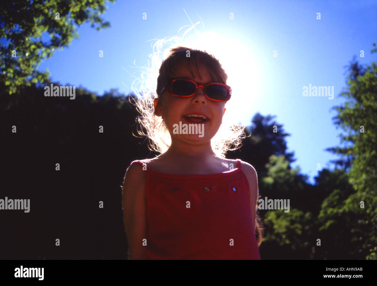 Girl smiling in sunglasses with the sun behind her creating a halo effect Stock Photo