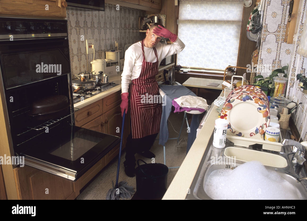 househusband struggling with housework trying to do three jobs at one in kitchen Stock Photo