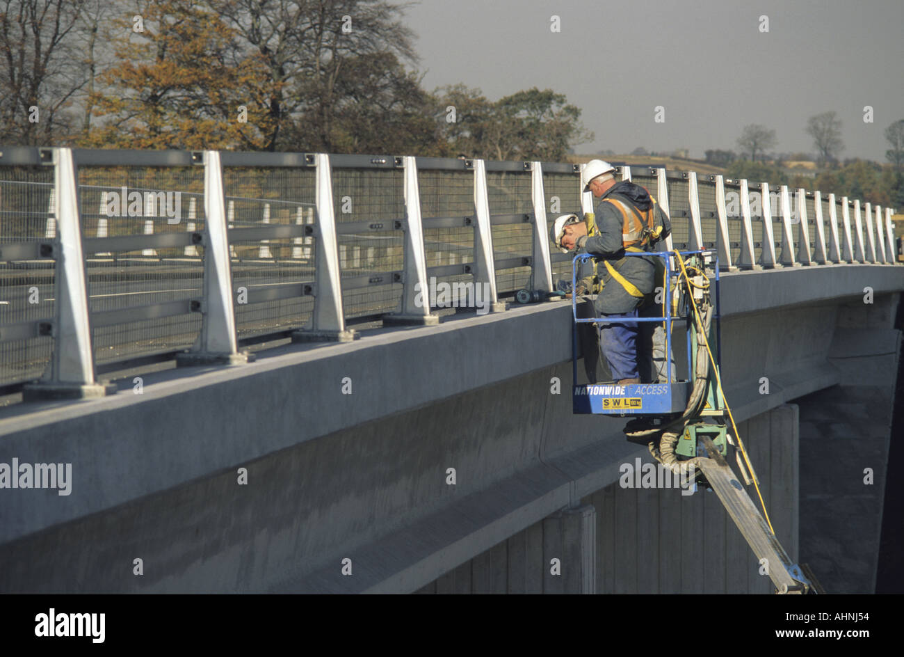 construction engineers using hydraulic hoist to work on bridge spanning ...