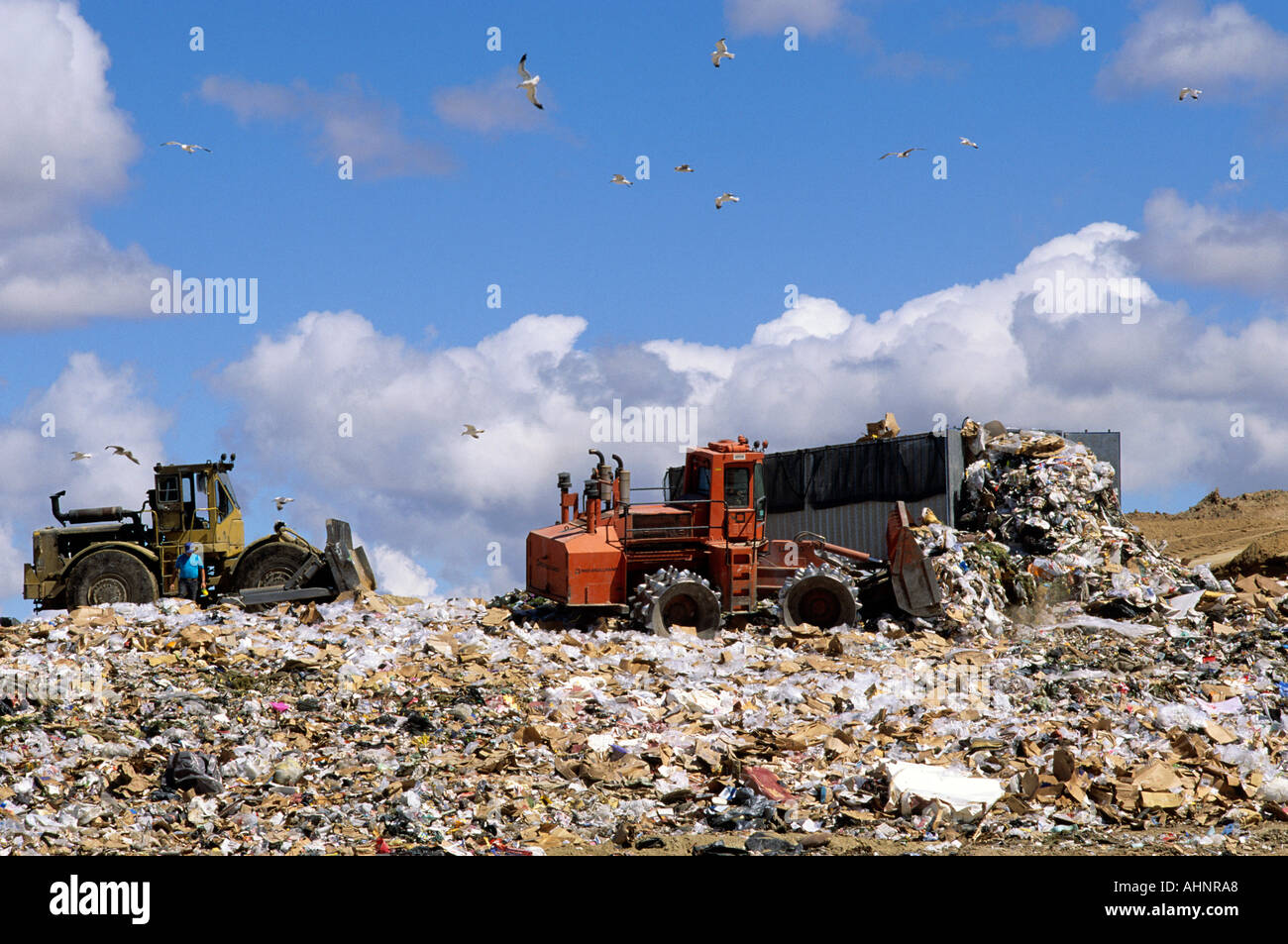 A large dumpster unloads trash while bulldozers move it at a sanitary