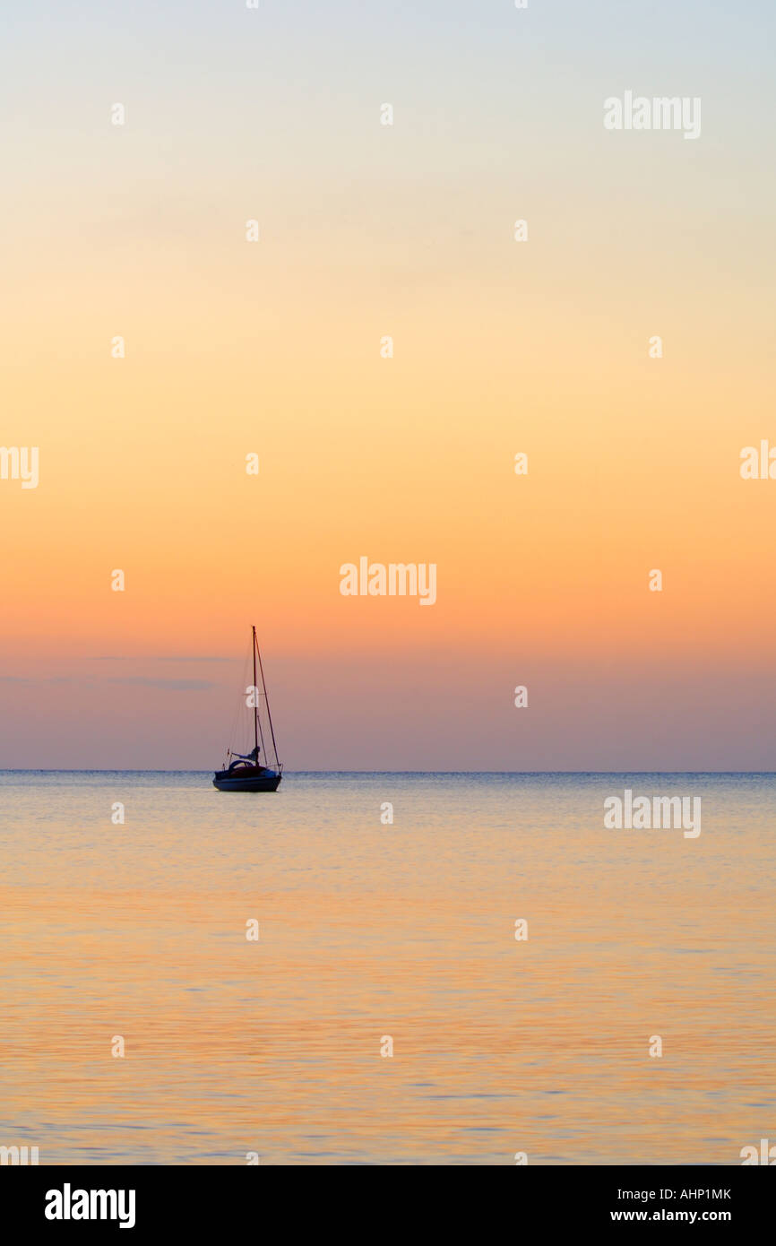 Sailing boat at anchor on a calm sea silhouetted against the orange glow of the rising sun Stock Photo