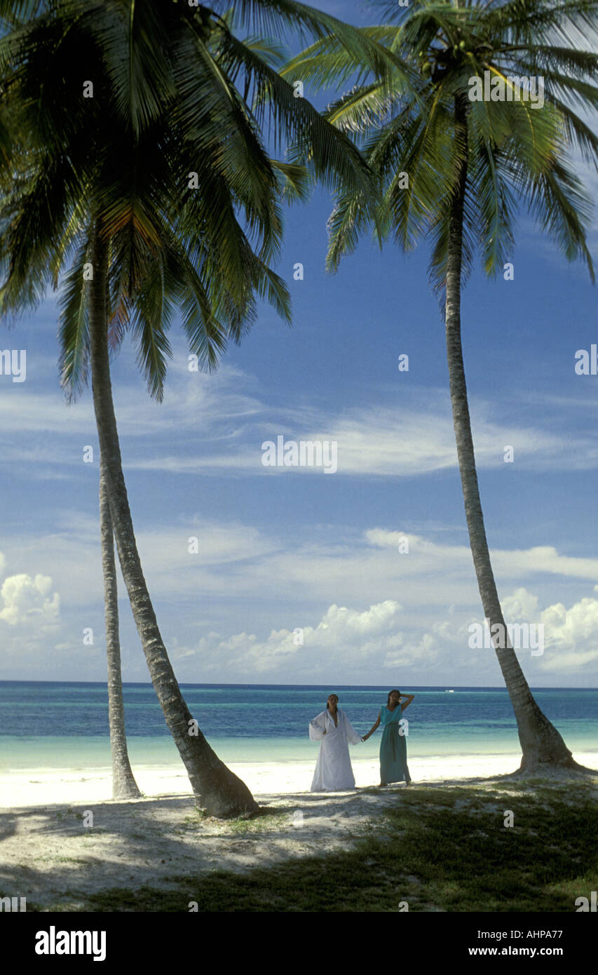 Two elegant women pose beneath tall graceful palm trees on Diani Beach Kenya East Africa Stock Photo