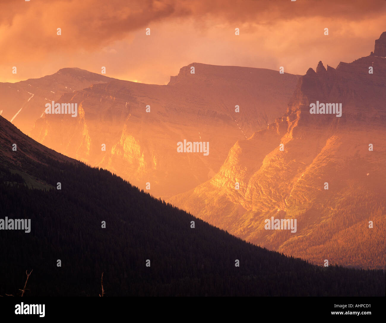 Sun peeking through clouds and shining on mountains of Glacier National ...