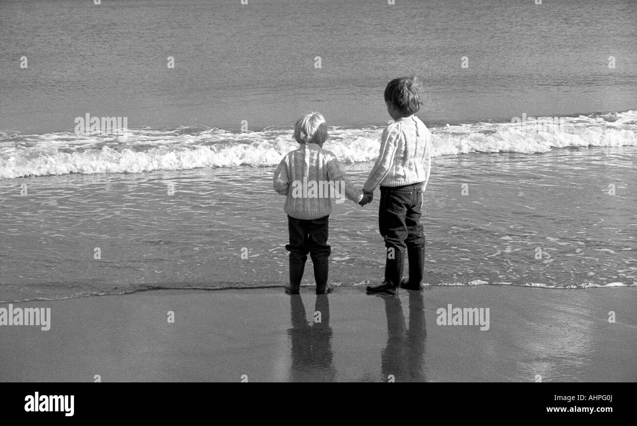 Two small boys on a beach at the waters edge on a bright day in winter. Stock Photo