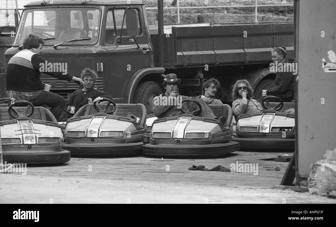 Group of male workers sitting in dodgem cars and eating at a work break. Stock Photo