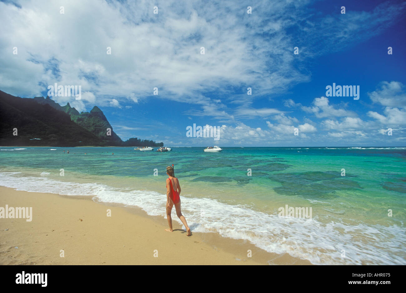 Woman walking on Tunnels beach (Makua Beach) with skindiving boats
