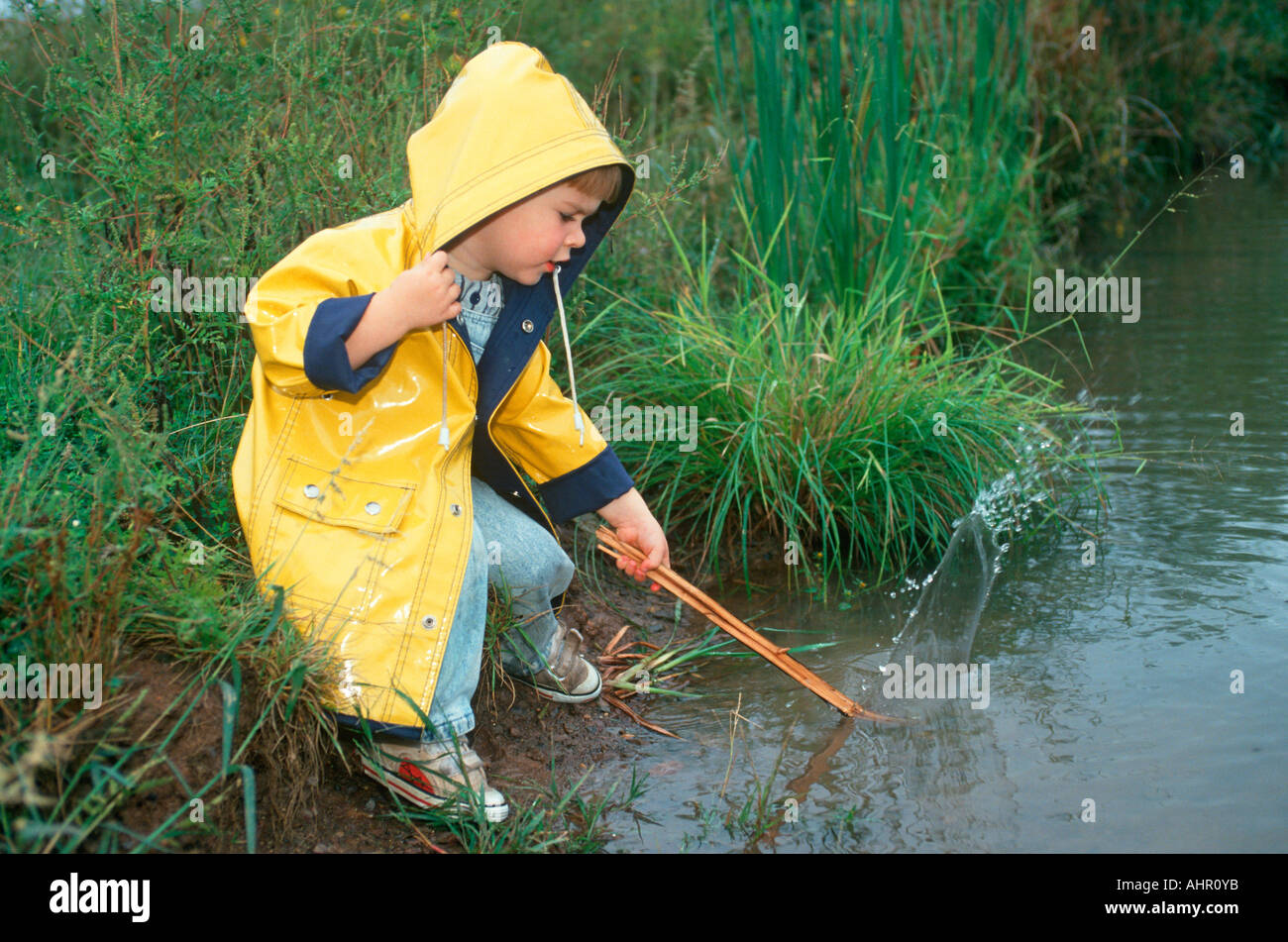 https://c8.alamy.com/comp/AHR0YB/little-boy-in-yellow-raincoat-playing-at-edge-of-a-stream-AHR0YB.jpg
