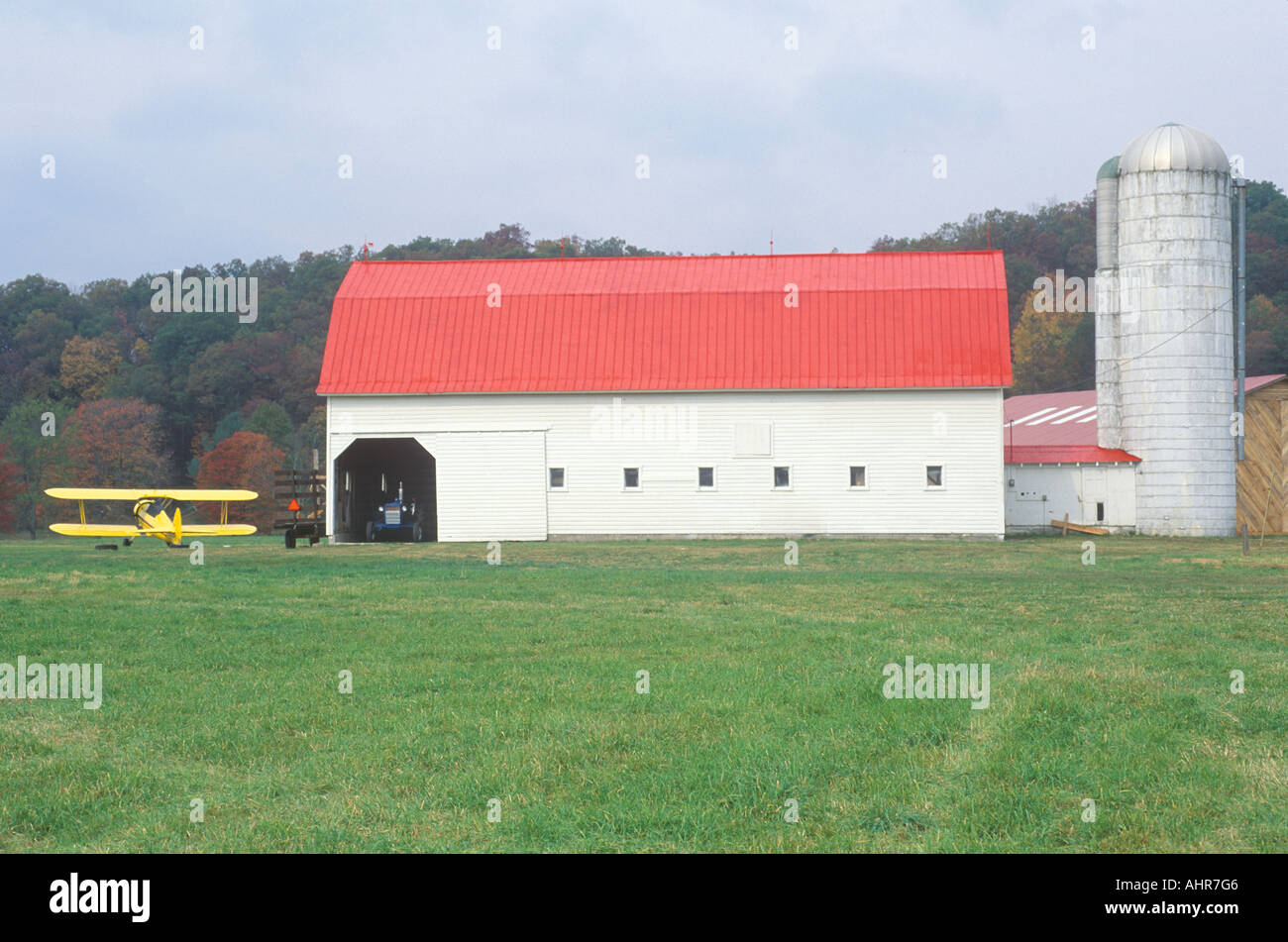 A yellow airplane red barn and grain silo on a farm in WV Stock Photo