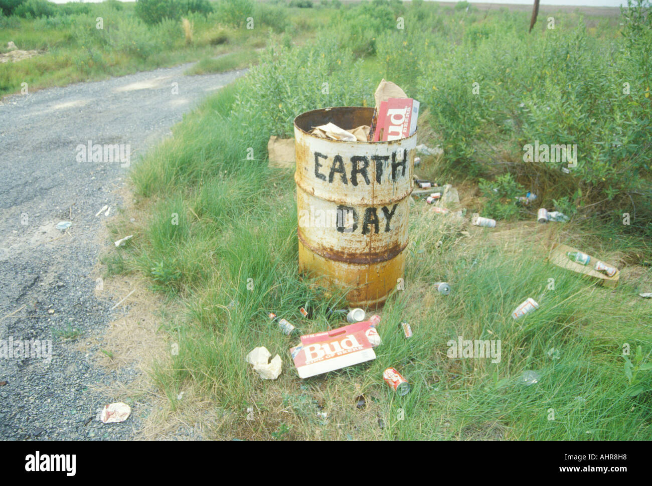 Cardboard beer cartons on the ground next to a trash can with the words Earth Day painted on its side Stock Photo
