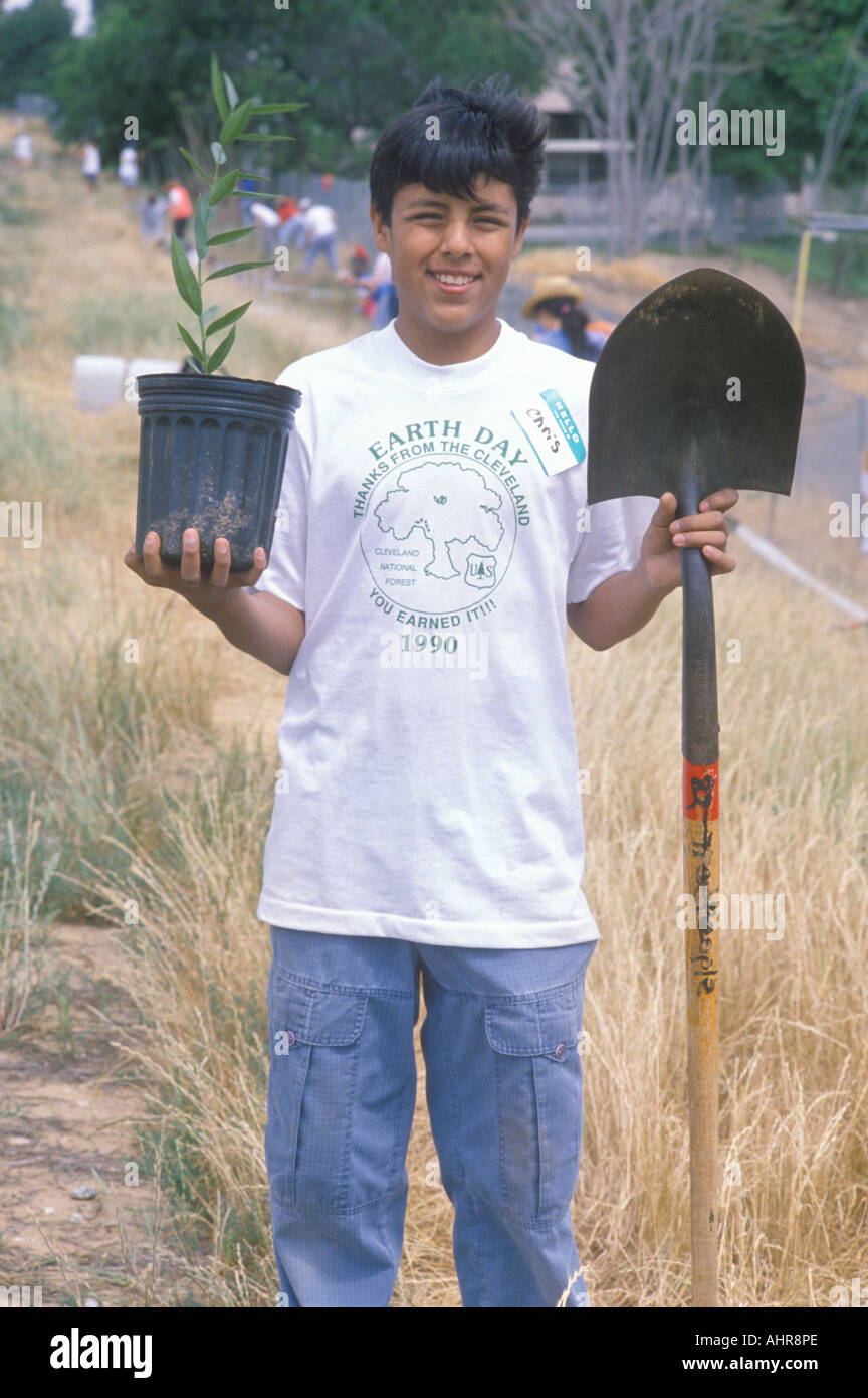 A teenage boy holding a plant and a shovel during Earth Day participation Stock Photo