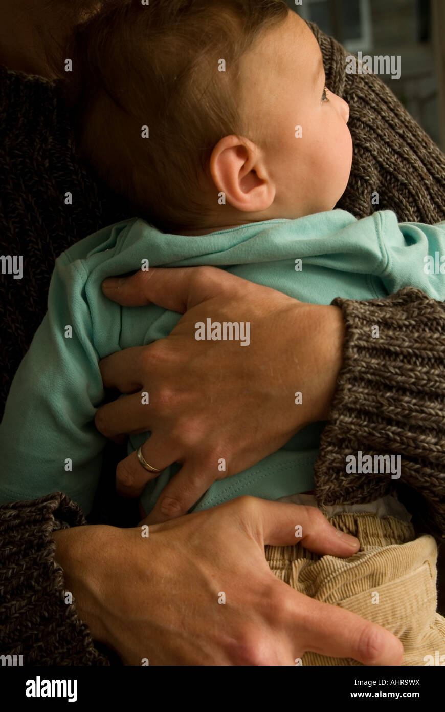 A father wearing the wedding ring holding his baby carefully with two delicate hands tight and firmly Stock Photo