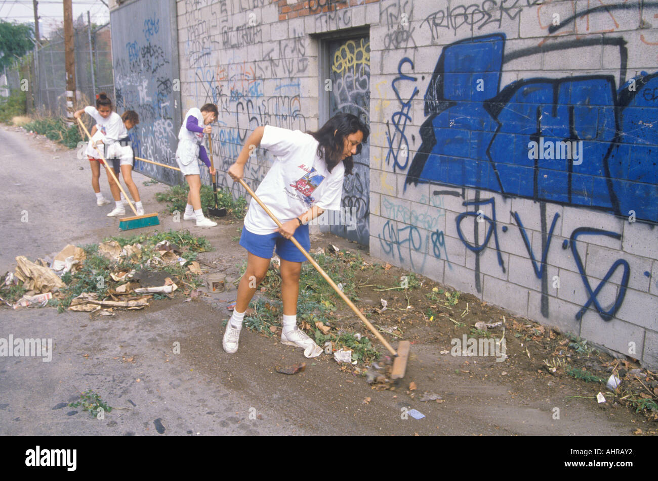 A group of young people participating in community cleanup by sweeping an alley Stock Photo