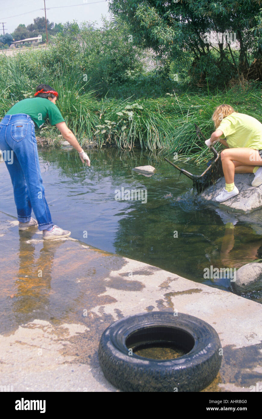 Two women working together to retrieve a chair from a small body of water Stock Photo