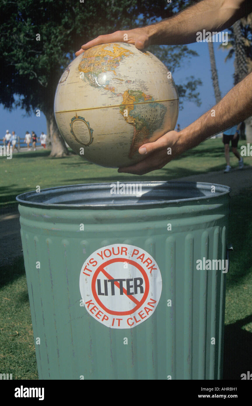 Hands holding a globe over a park trash receptacle Stock Photo