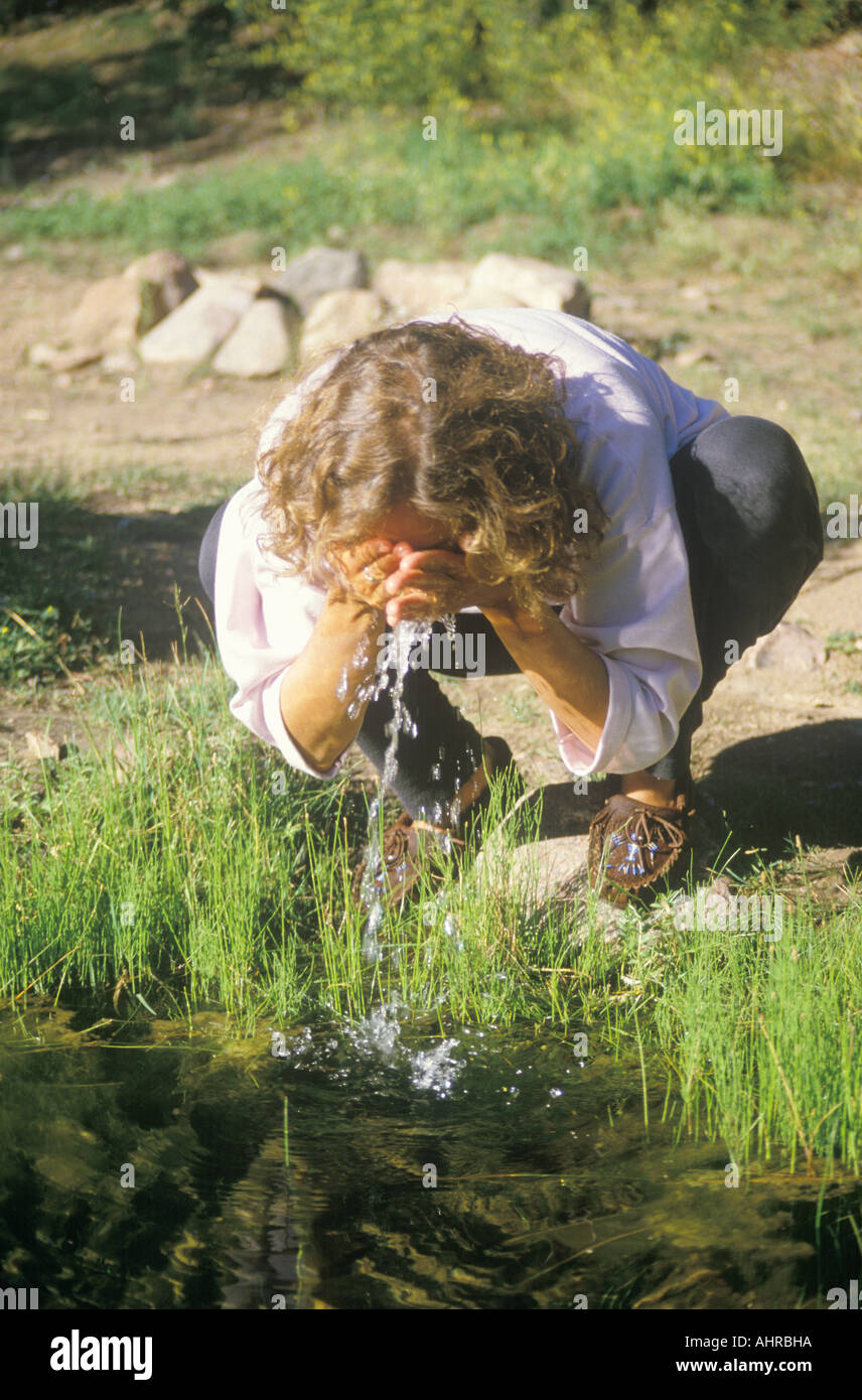 Woman splashing some clean water on her face from a river Stock Photo