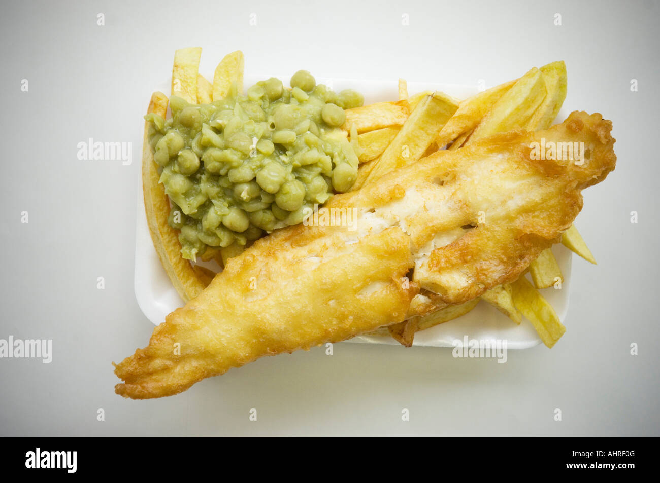 Fish chips and peas in a plastic tray on neutral background Stock Photo