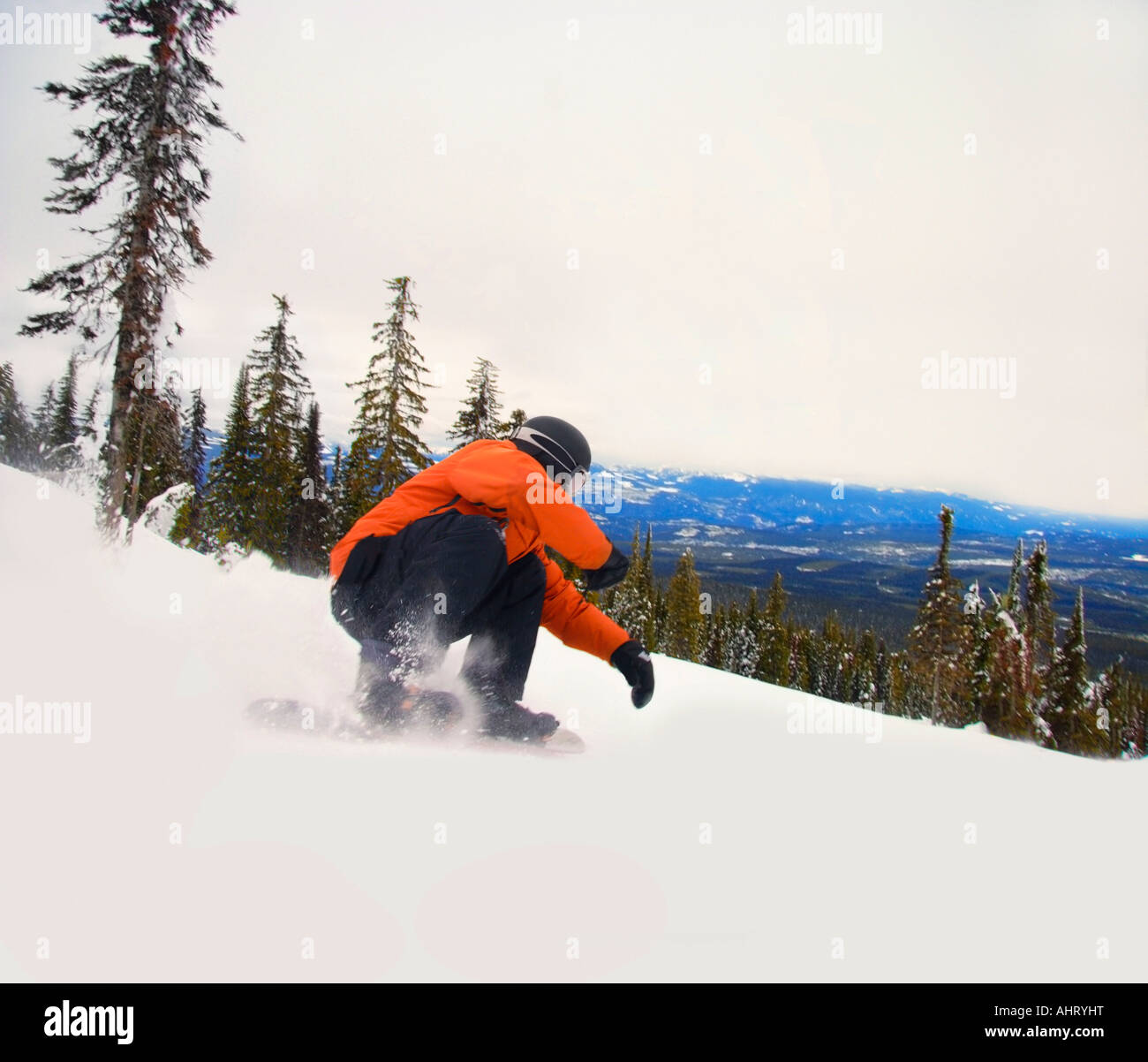Snowboarder crouching down low as he descends snow hill Stock Photo