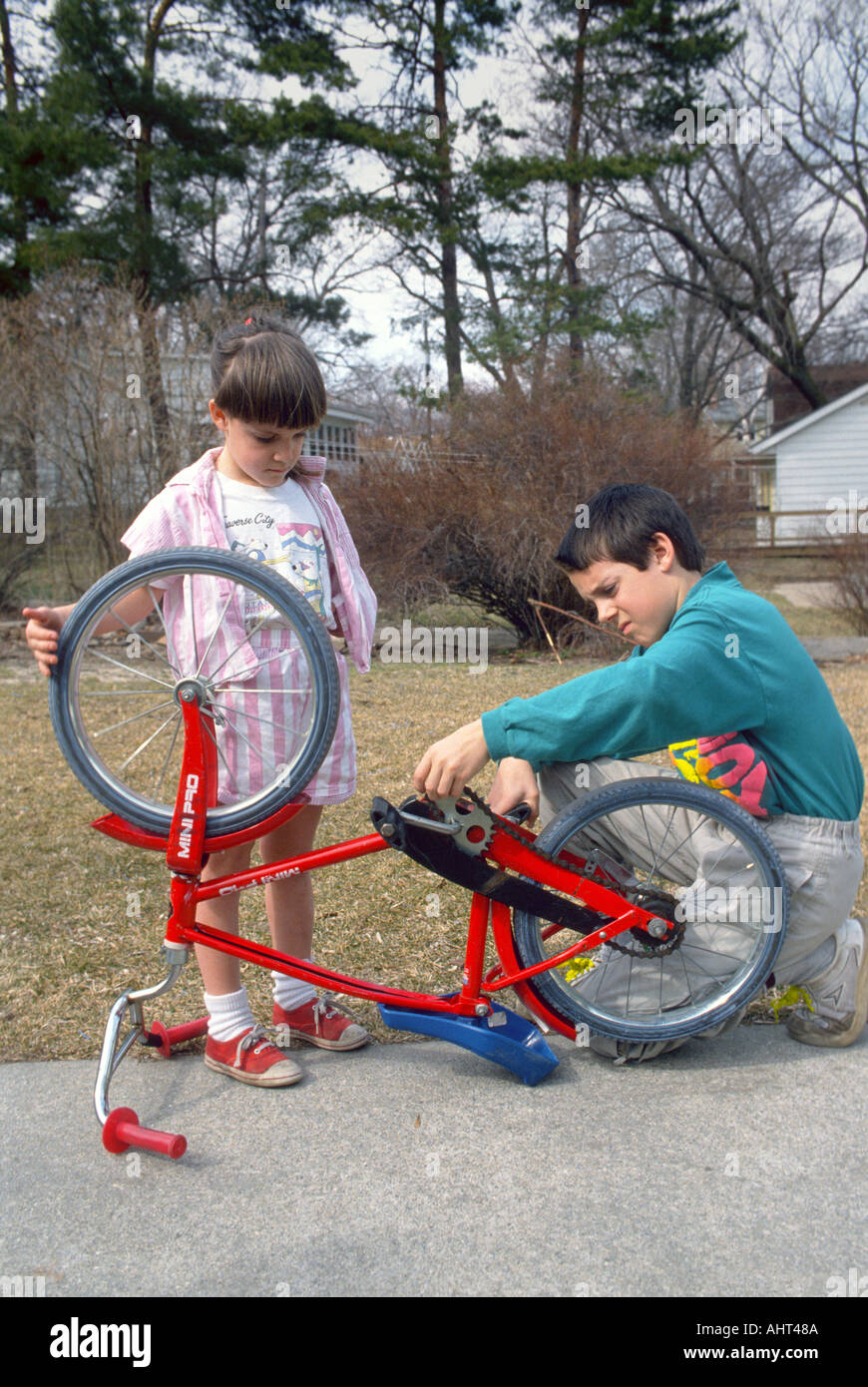 Brother helps younger sister fix a loose chain on her bicycle Stock