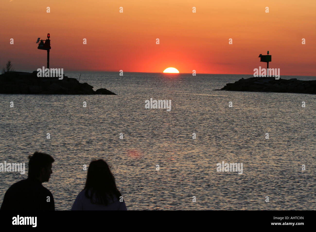 Couple with their back turned away from the camera, watching a beautiful sunset over a harbor Stock Photo