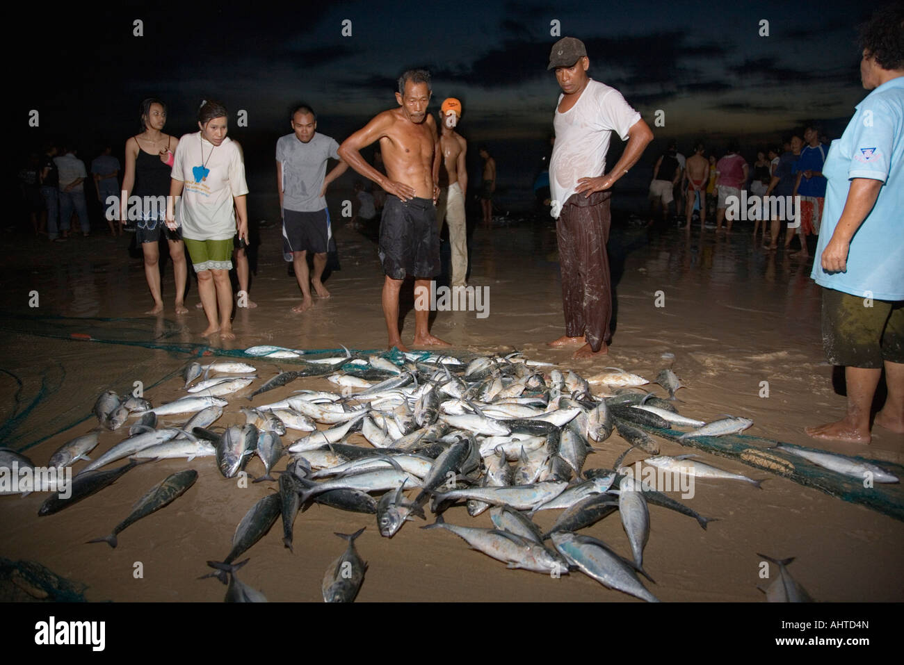 Artisan fishermen contemplate their fish catch at dusk, Nai Harn Beach, Phuket Island, Thailand Stock Photo