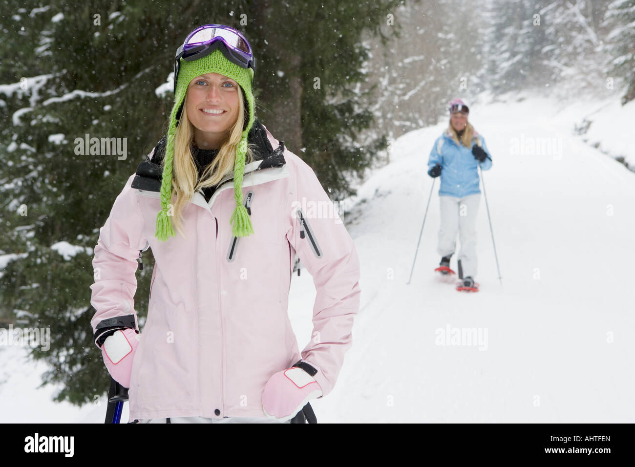 Young woman smiling on ski-slope, person in background on snow-shoes, portrait Stock Photo