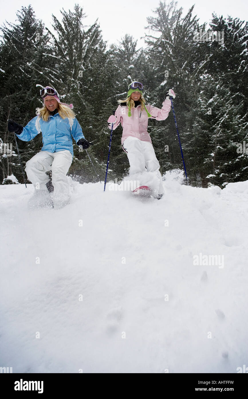 Low angle view of two young blonde women walking down small hill in forest using snow-shoes Stock Photo